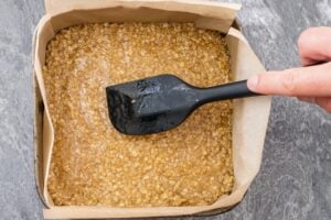 Patting down the flapjack mixture flat with a black spatula